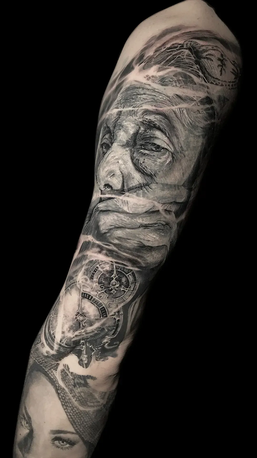 Tatuaje en el brazo, negro y gris. Retrato de una persona, calavera y otros elementos abstractos.