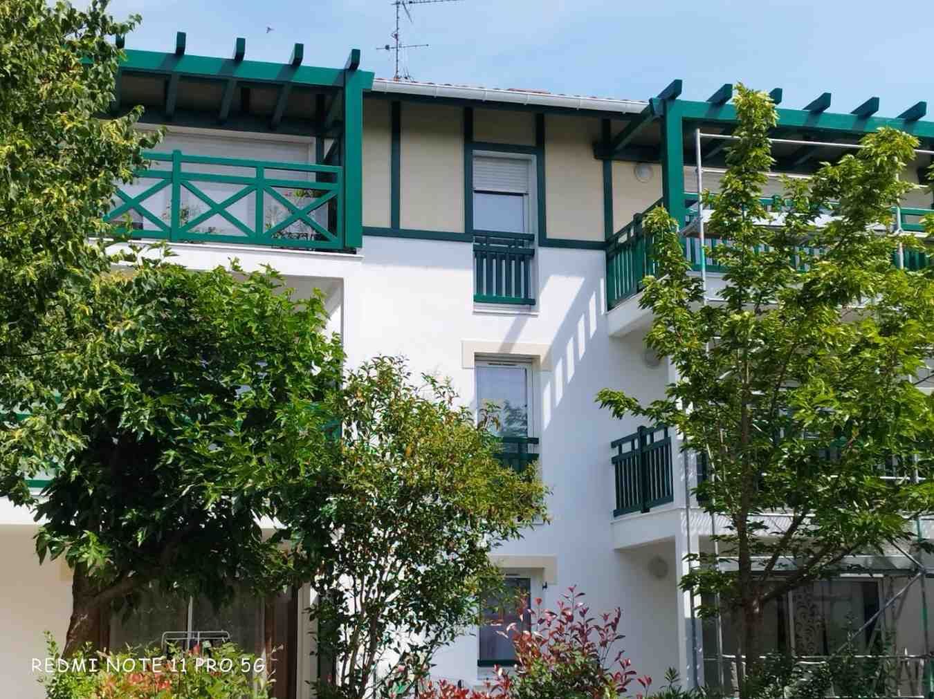 Edificio blanco con detalles verdes, balcones y árboles.