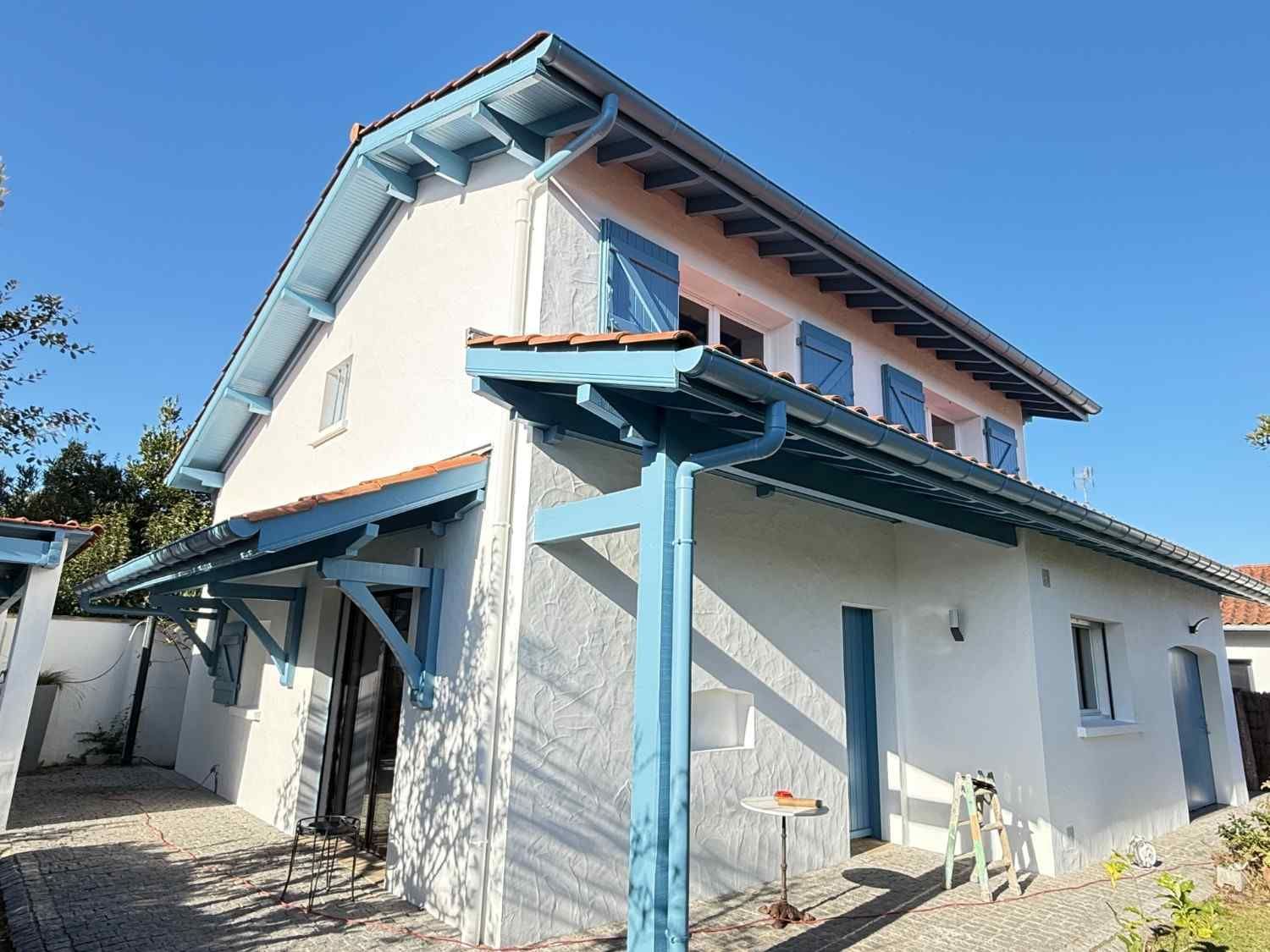 Casa de dos pisos con paredes de estuco claro, molduras azules y contraventanas azules contra un cielo despejado.