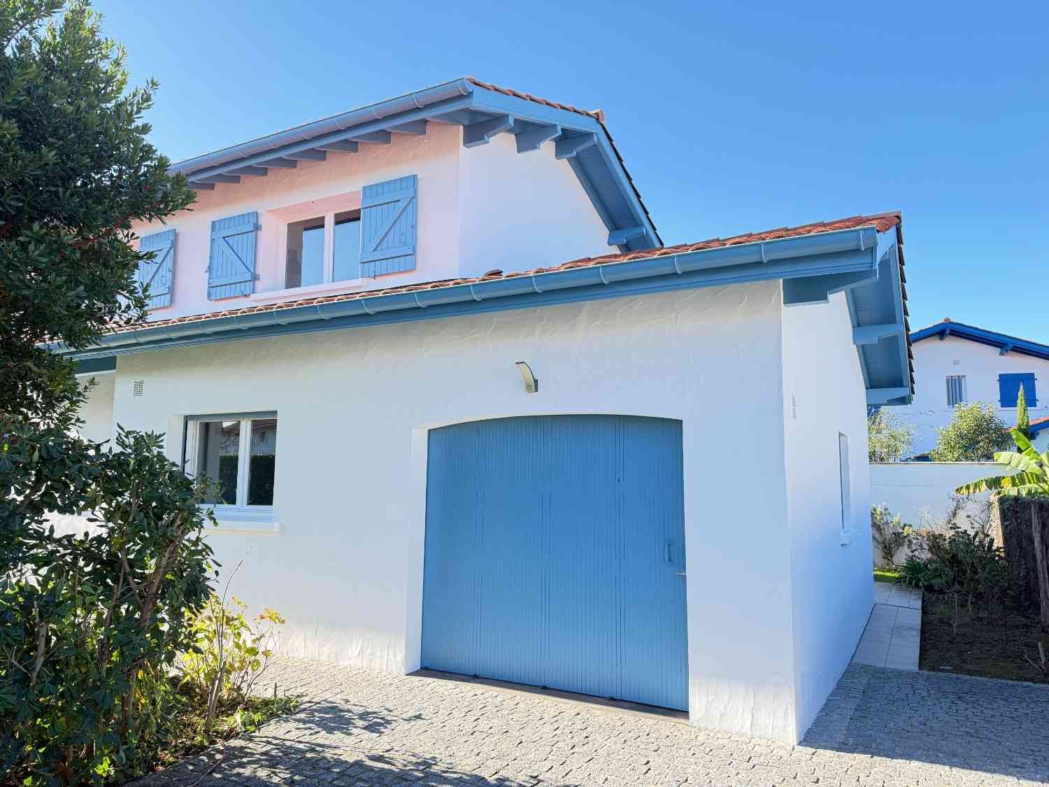 Casa blanca con persianas, puerta y molduras azules bajo un cielo azul claro.