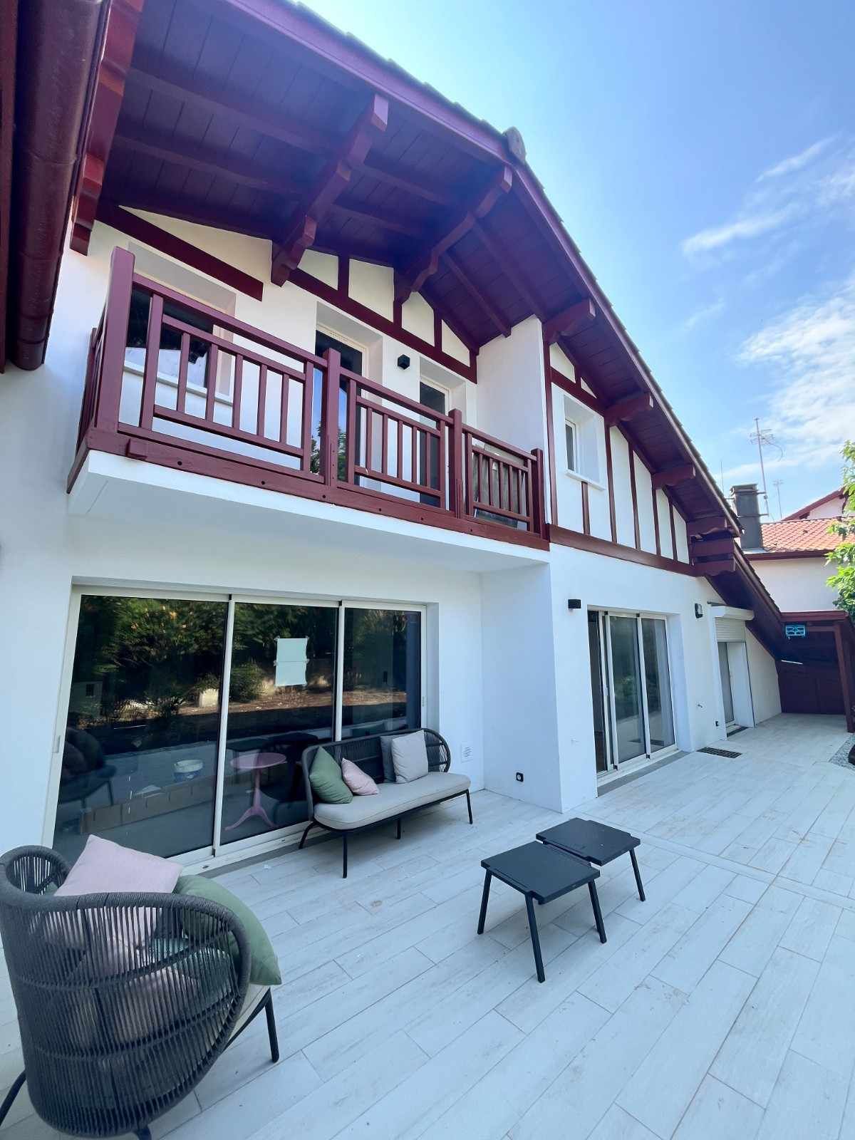Casa blanca con detalles rojos, balcón y muebles de patio en un día soleado.