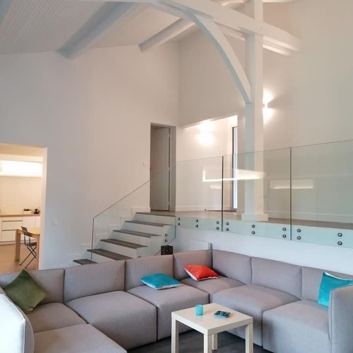 Moderna sala de estar con sofá seccional, barandilla de vidrio y vigas a la vista.