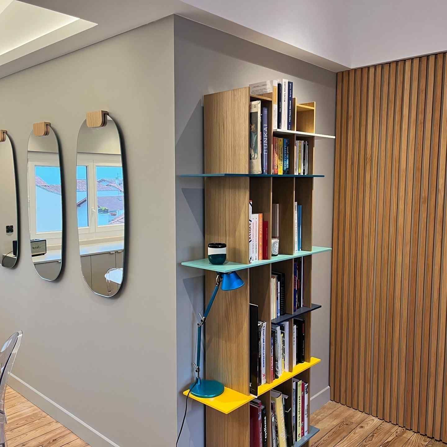 Espacio habitable moderno con estantería, espejos y pared revestida de madera.