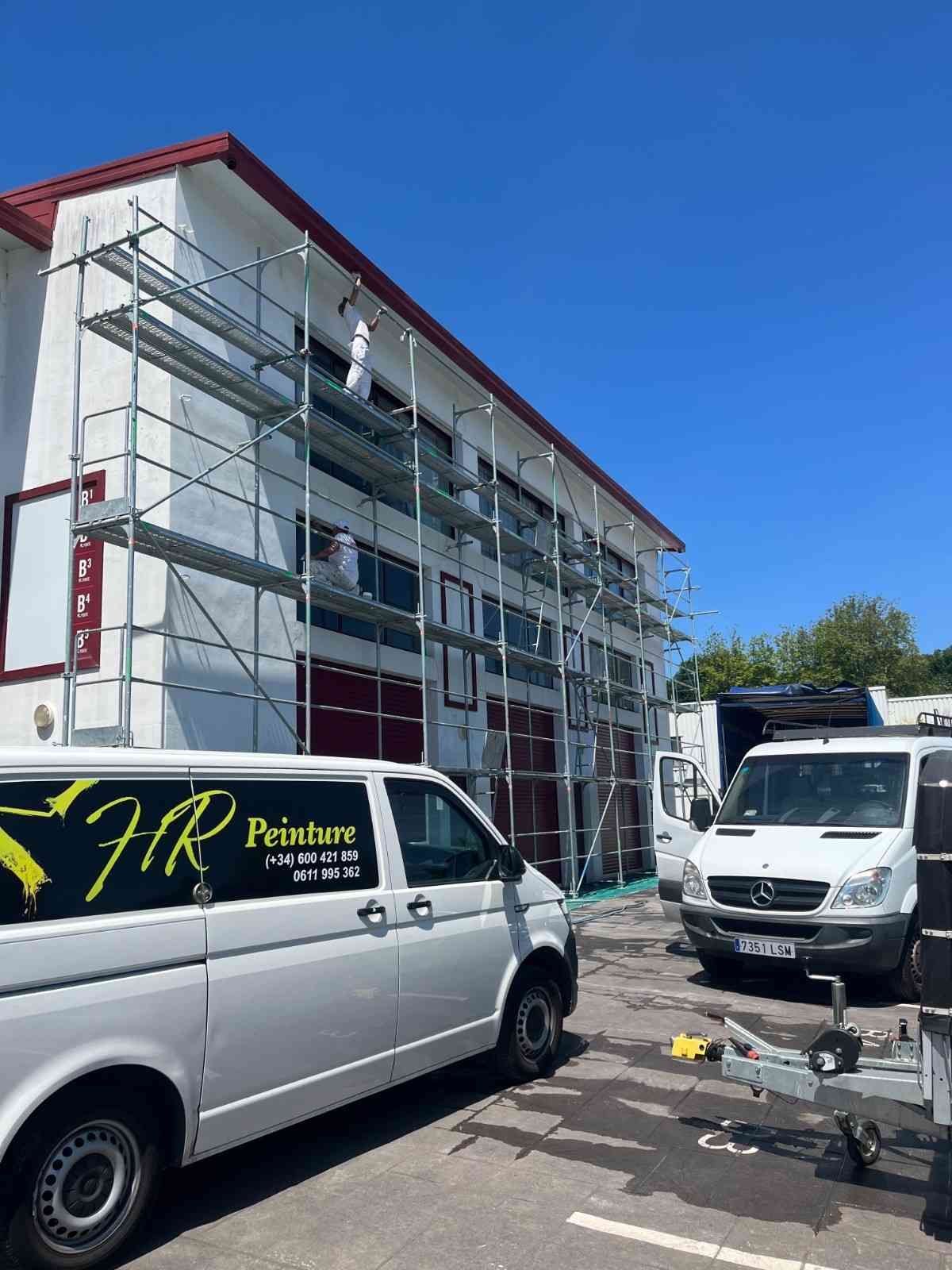 Un edificio con andamios, dos furgonetas blancas y un cielo azul claro.