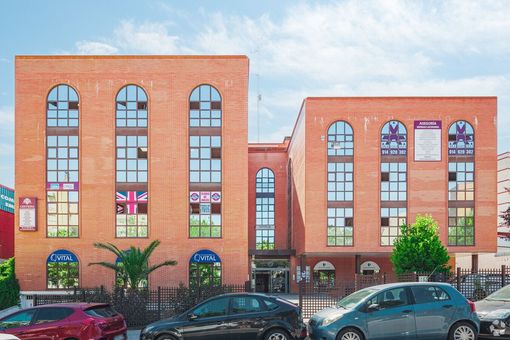 Edificio de ladrillo con altas ventanas arqueadas y coches aparcados delante.