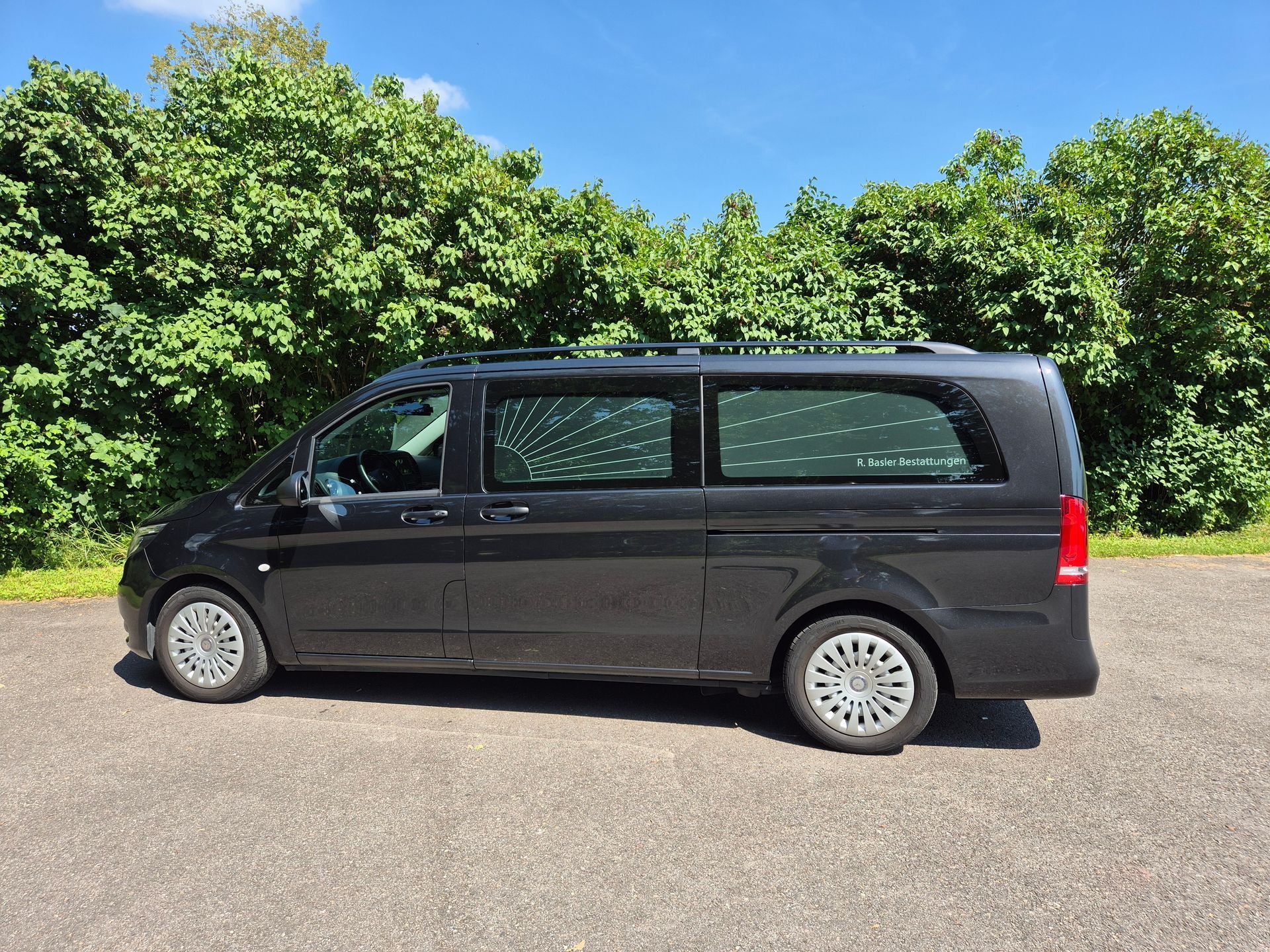 Ein schwarzer Lieferwagen steht auf einem Parkplatz, im Hintergrund sind Bäume zu sehen.