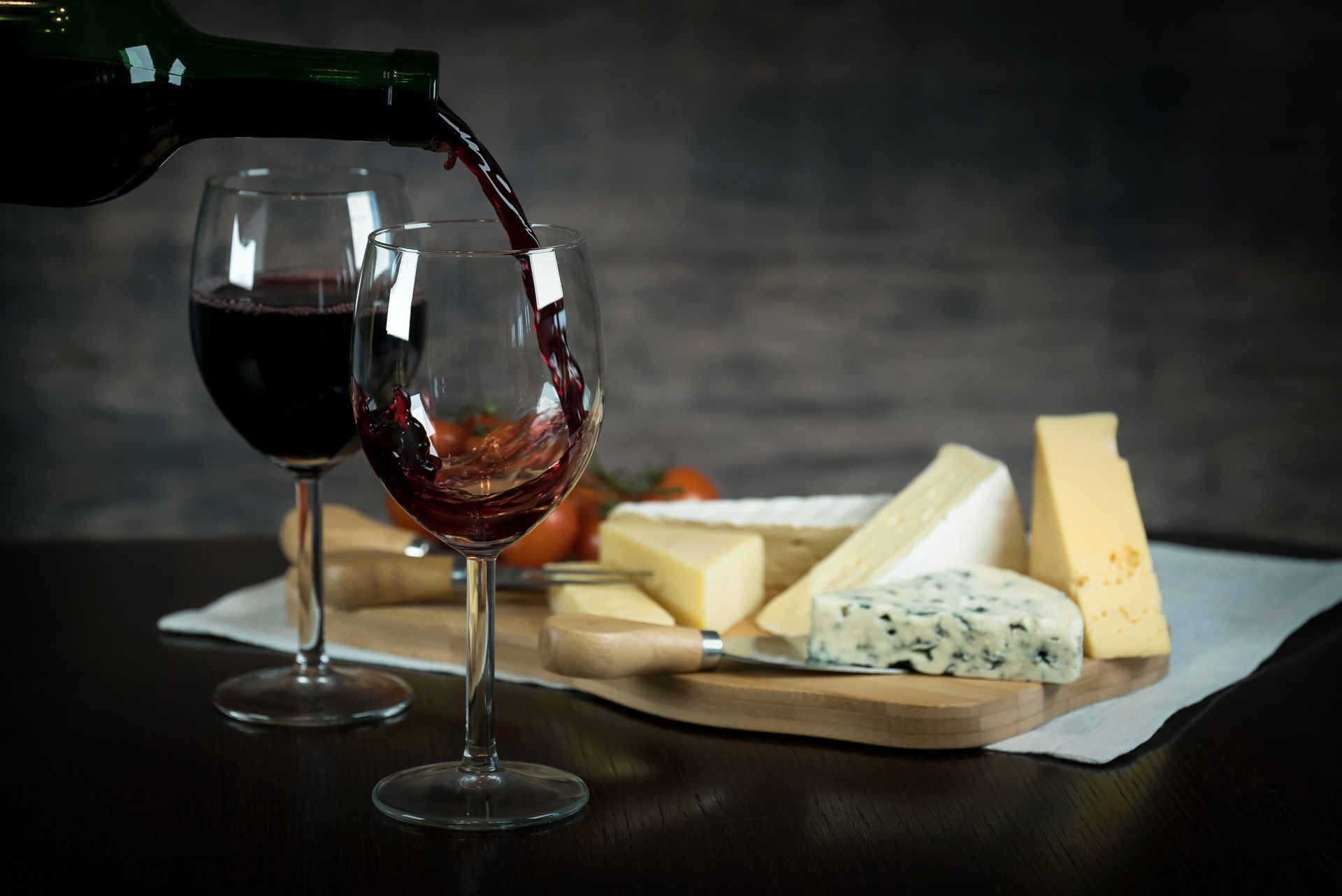 Rotwein wird in ein Glas eingeschenkt, dazu eine Käseauswahl auf einem Holzbrett.