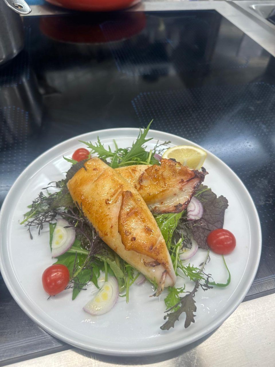 Gegrillter, gefüllter Tintenfisch mit Gemüse, Kirschtomaten und Zitrone auf einem Teller.