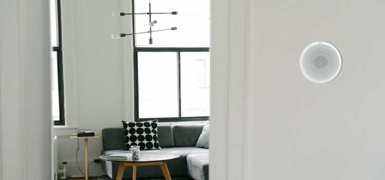 Habitación blanca con un altavoz montado en la pared y una sala de estar visible al fondo.