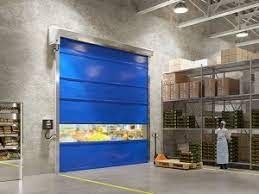 Puerta rápida azul en un almacén, con una persona de pie cerca de estanterías llenas de productos envasados.