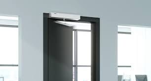 Abrepuertas automático instalado sobre una puerta oscura en un entorno de oficina moderno.