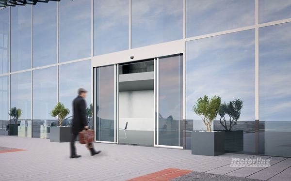 Una persona pasa a través de una puerta corrediza automática de vidrio hacia un edificio moderno.