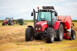 Un tractor rojo está empacando heno en un campo.