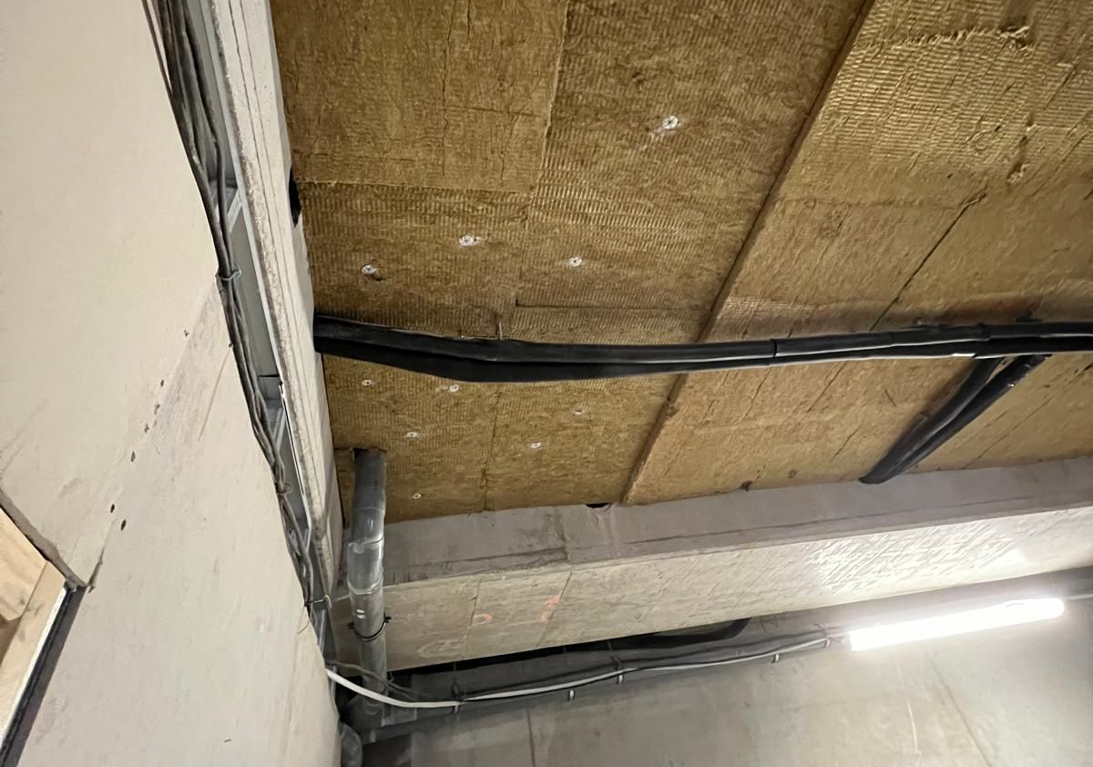 Plafond en construction : isolation, conduits électriques, ossature métallique contre le béton et mur.