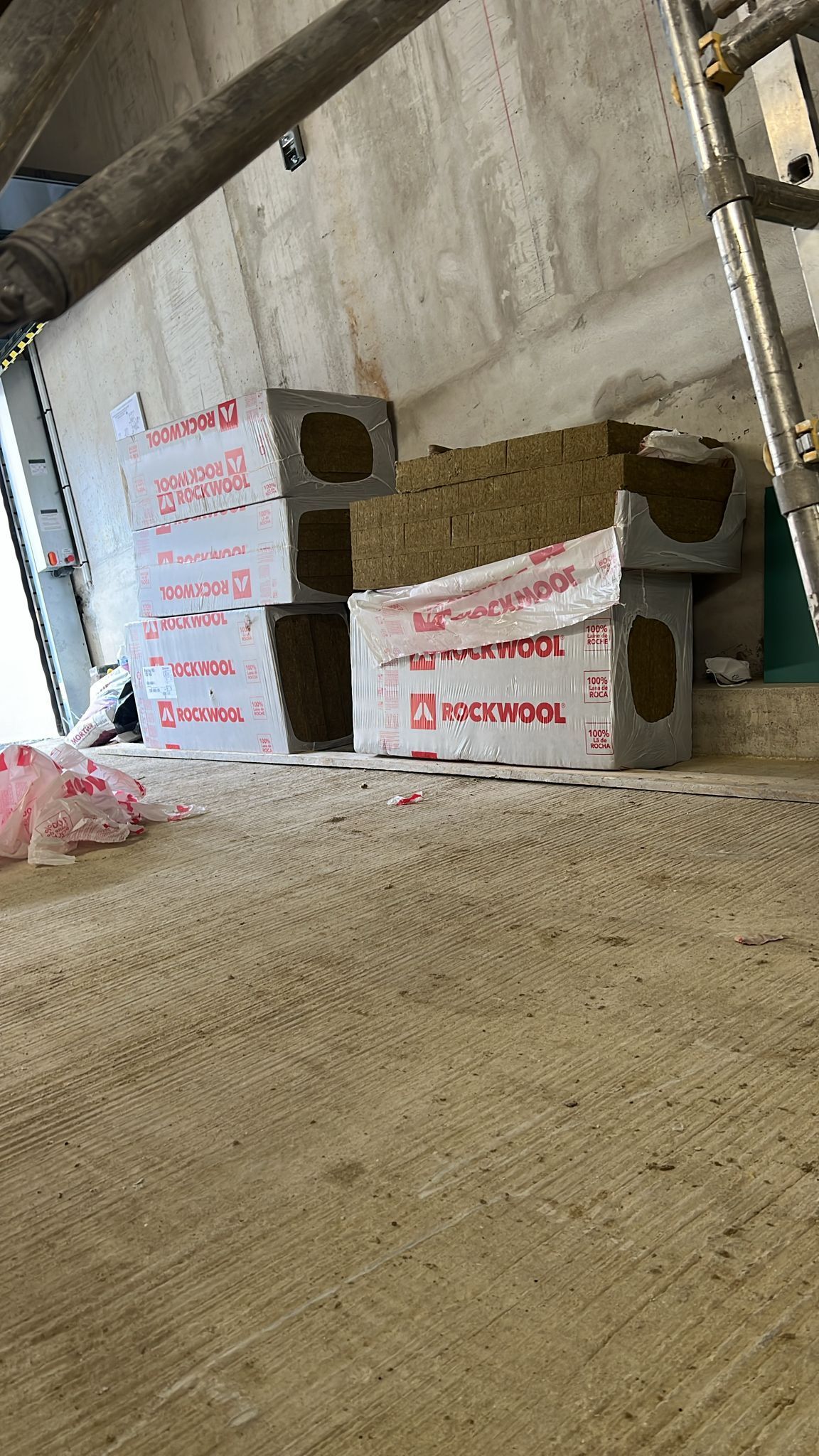 Intérieur d'un chantier : matériaux isolants, parpaings empilés et échelle.