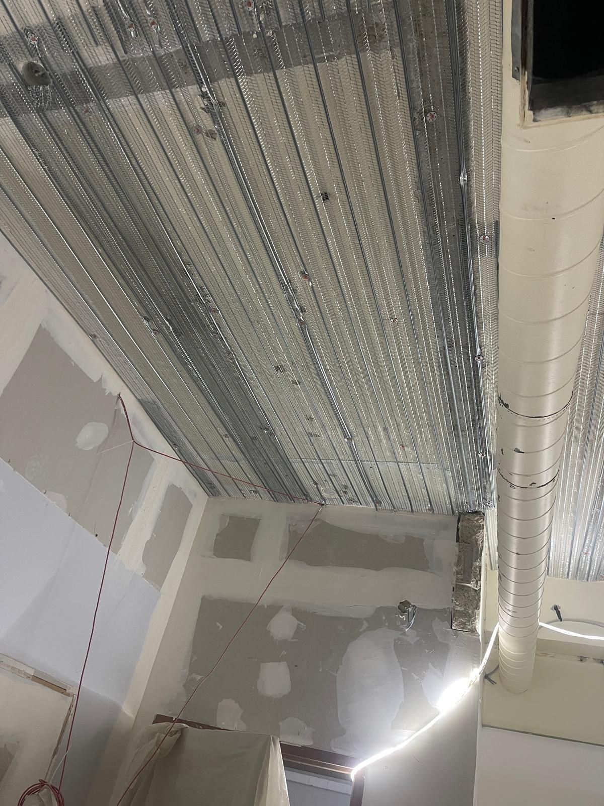 Plafond avec ossature métallique et conduits blancs installés dans une pièce en construction.