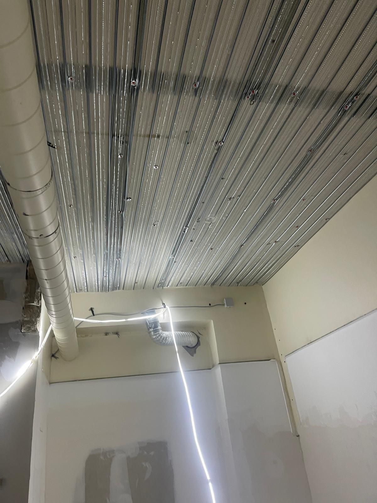 Plafond avec ossature métallique et conduits de ventilation. Murs partiellement finis visibles en dessous.