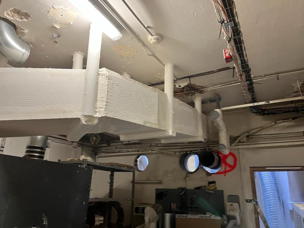 Conduits de ventilation, tuyaux, câbles et autres équipements mécaniques blancs au plafond, dans un environnement industriel.