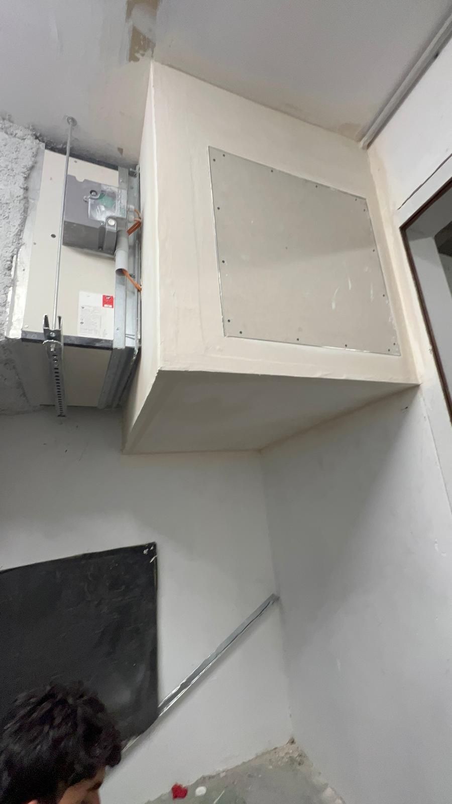 Panneau mural encastré ; unité de climatisation visible. Personne en bas. Couleurs : blanc et gris.