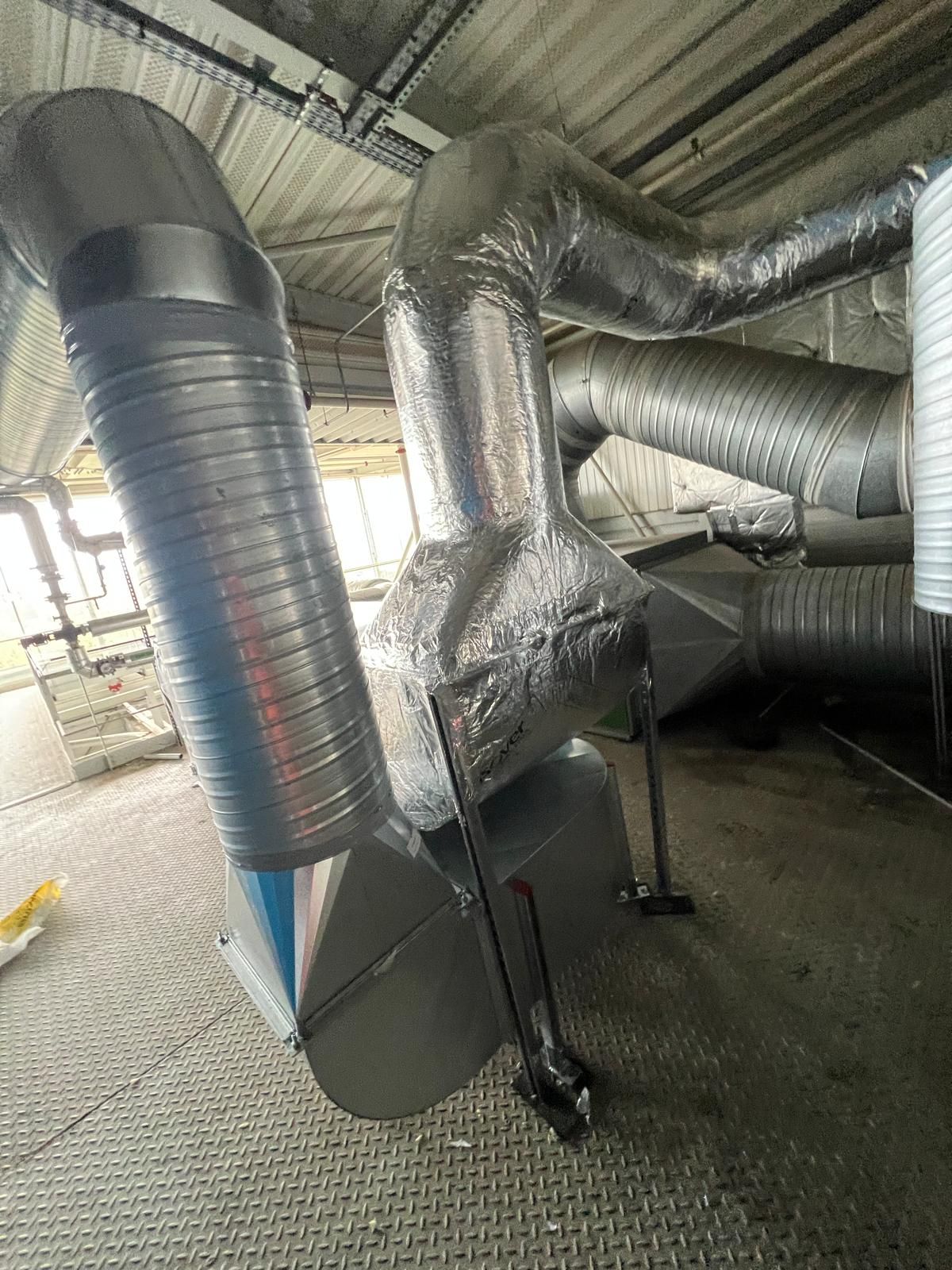 Conduits de ventilation, métalliques et isolés, sur une plateforme métallique, près du plafond d'un bâtiment.