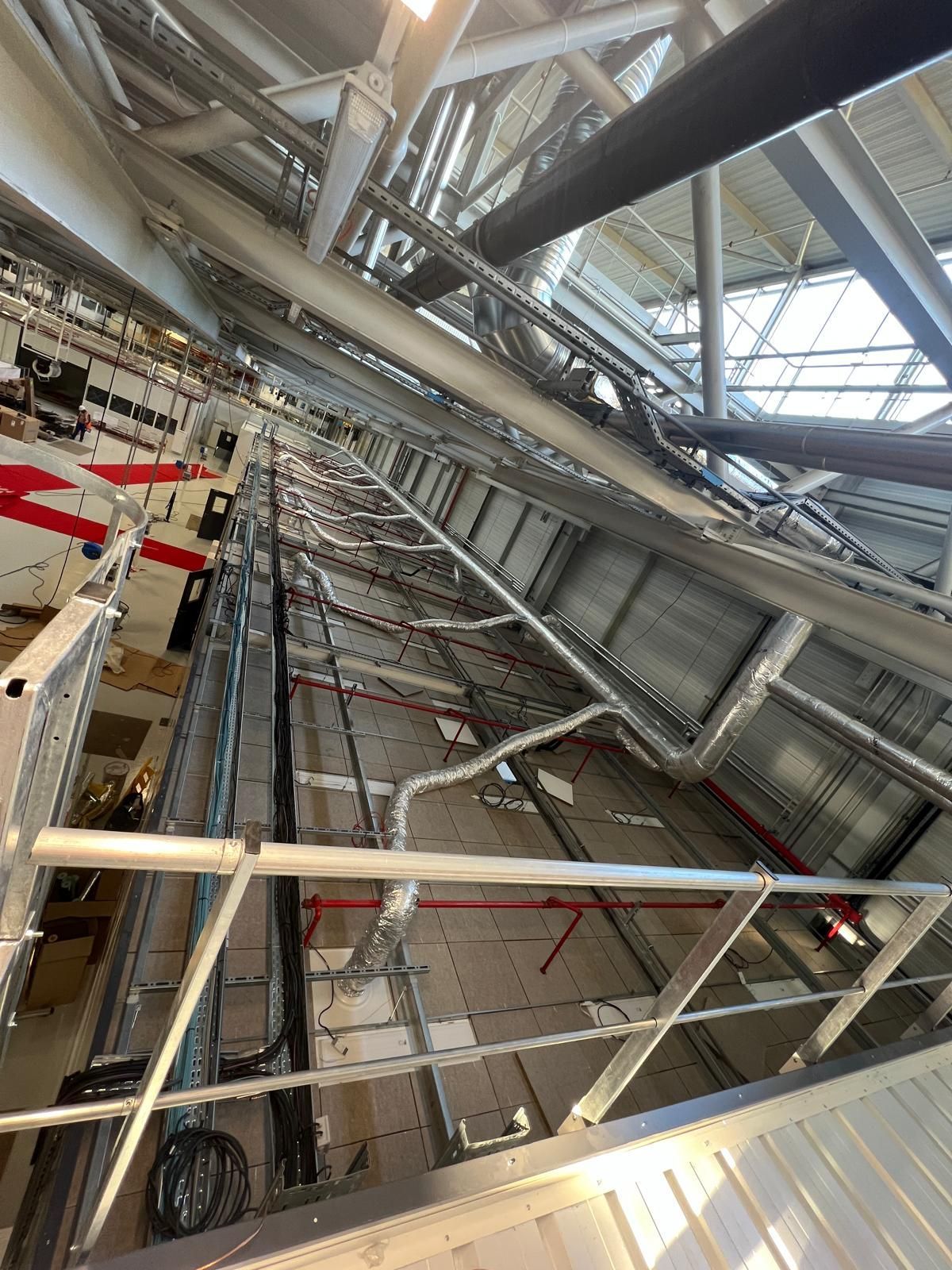 Intérieur industriel avec échelles, tuyaux et câbles longeant un haut mur.
