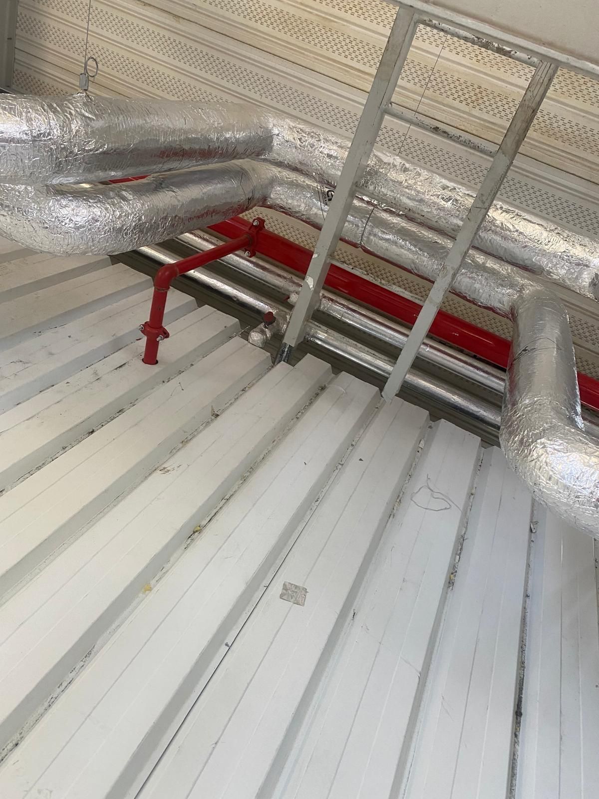 Des tuyaux métalliques et une échelle et une structure en tôle ondulée blanche.