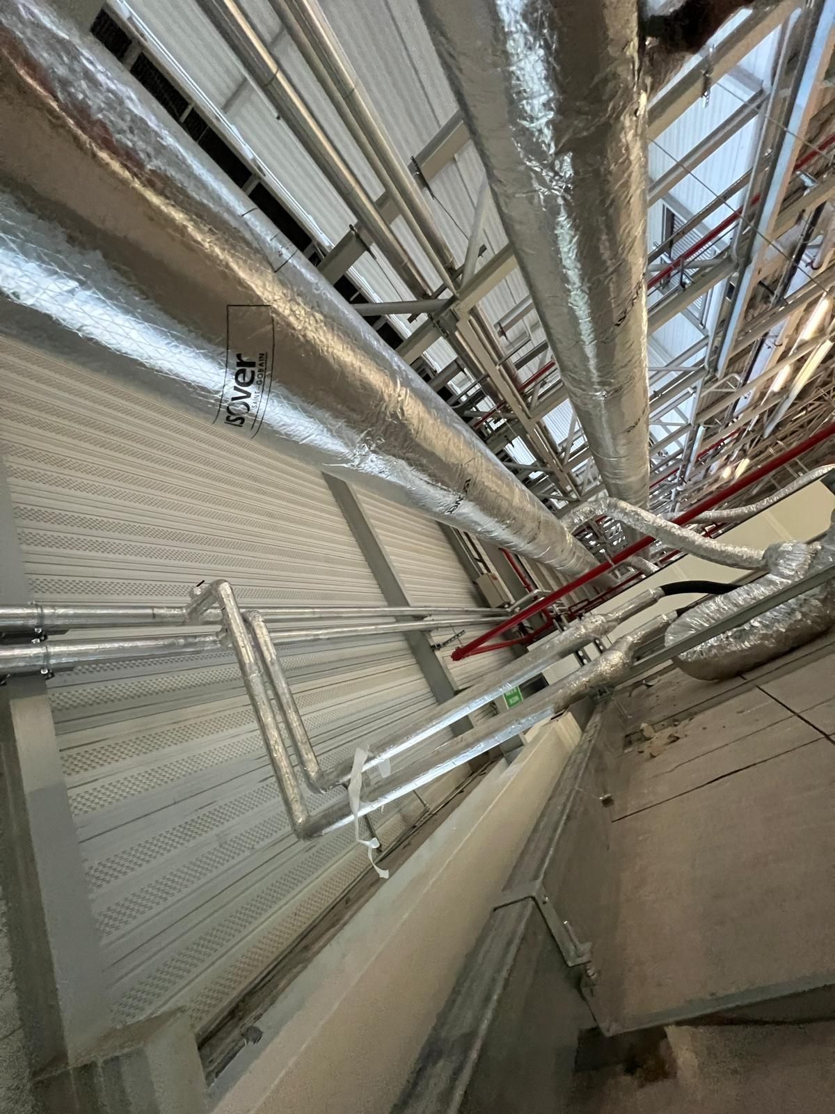 Tuyaux recouverts d'un isolant argenté qui longent des supports de plafond.