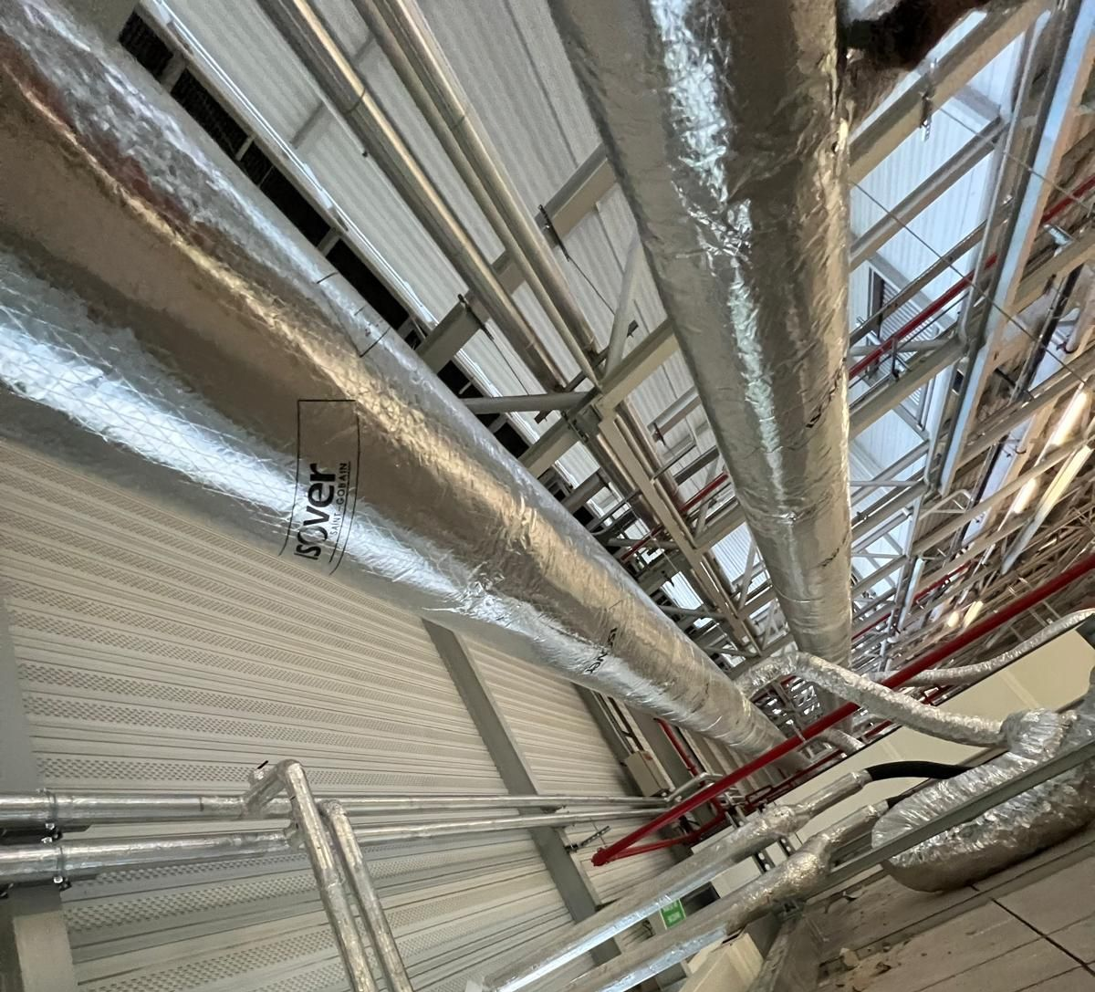 Canalisations isolées dans un bâtiment commercial. Revêtement argenté, canalisations rouges, murs et plafond blancs.