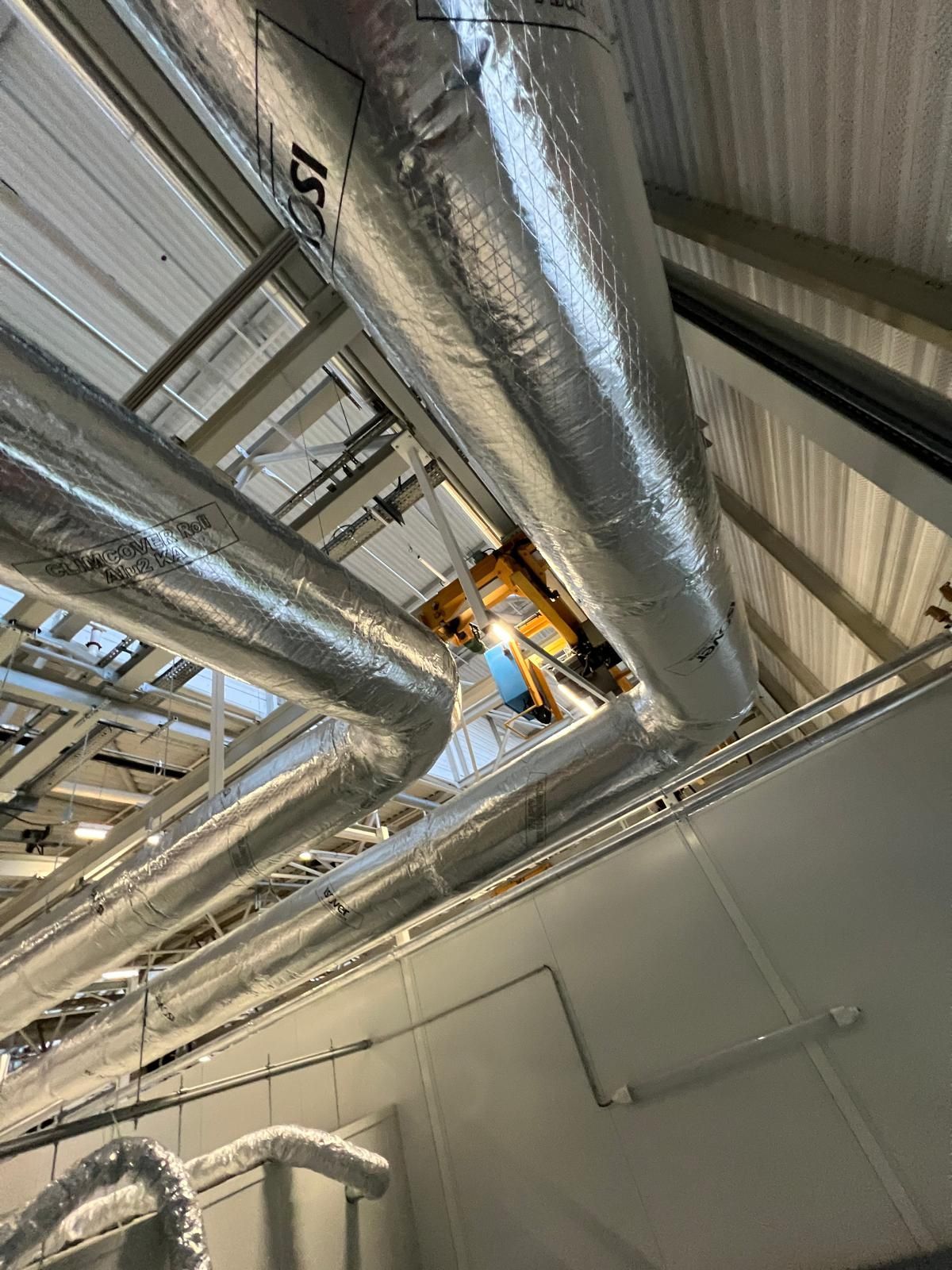 Des tuyaux isolés le long d'un plafond, équipements techniques et charpente du bâtiment.