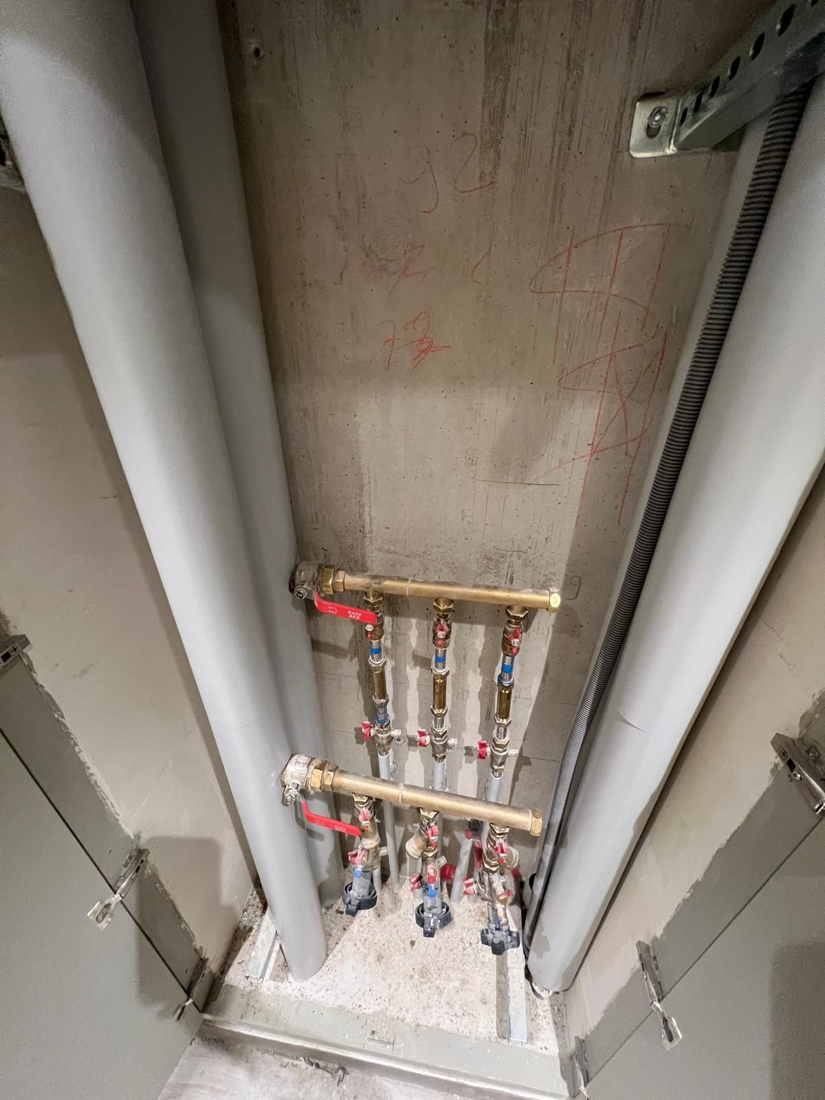 Tuyaux et vannes encastrés dans une niche murale, avec isolation. Tuyaux en laiton, vannes rouges et argentées, mur en béton.