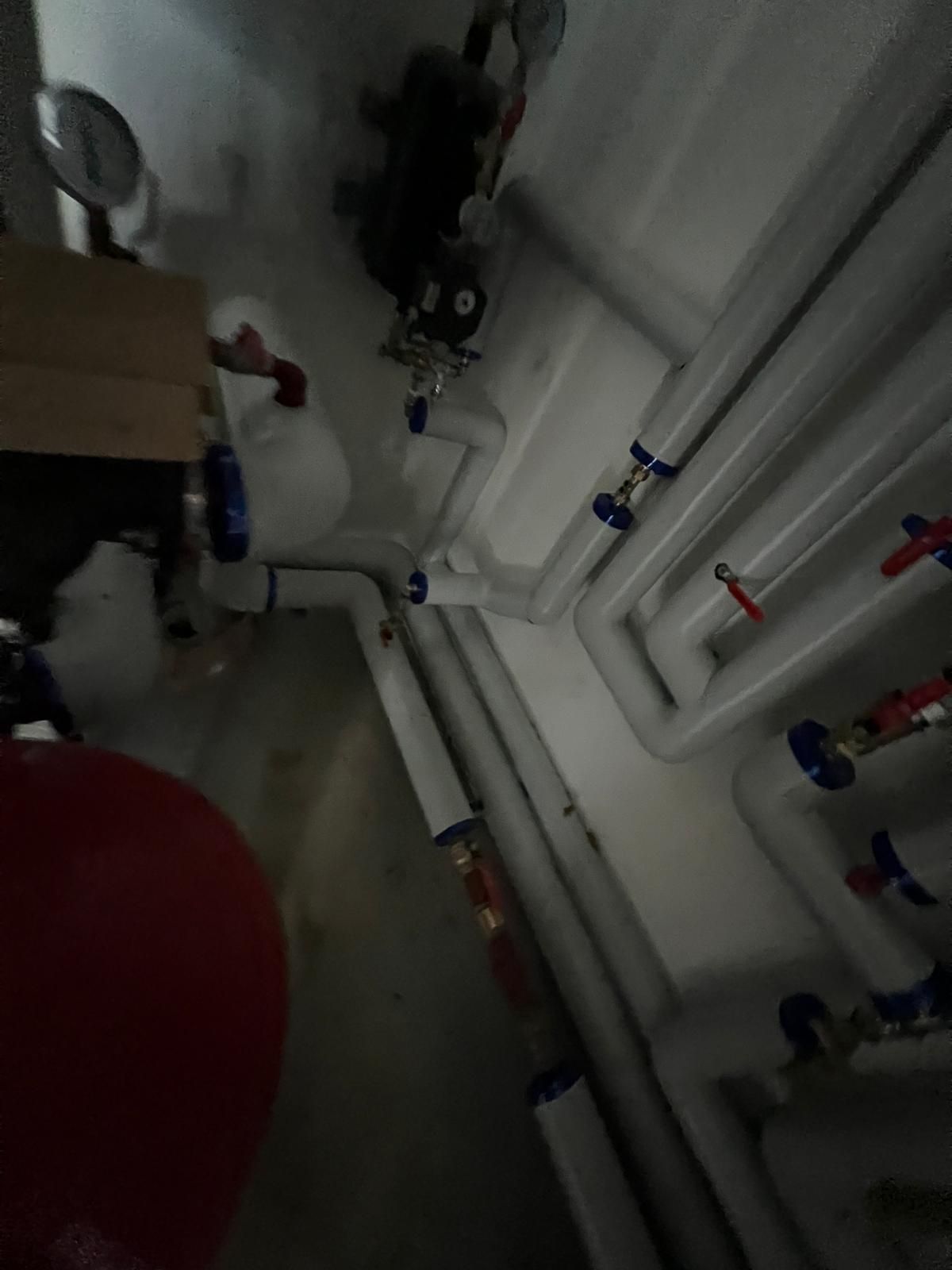 Tuyauterie et vannes dans un local technique. Tuyaux blancs, vannes bleues et rouges, réservoir rouge.