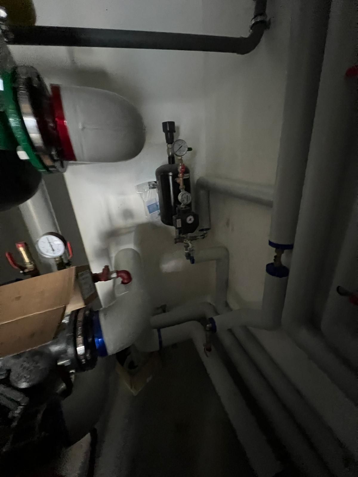 Système de tuyauterie dans un local technique. Tuyaux blancs et noirs avec manomètres et vannes. Espace sombre et clos.