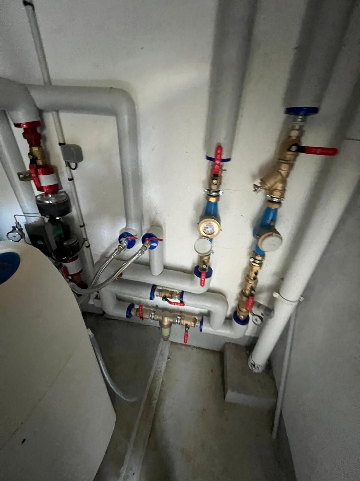 Tuyaux, vannes et manomètres dans un local technique. Tuyaux gris, vannes bleues et rouges sur un mur blanc.