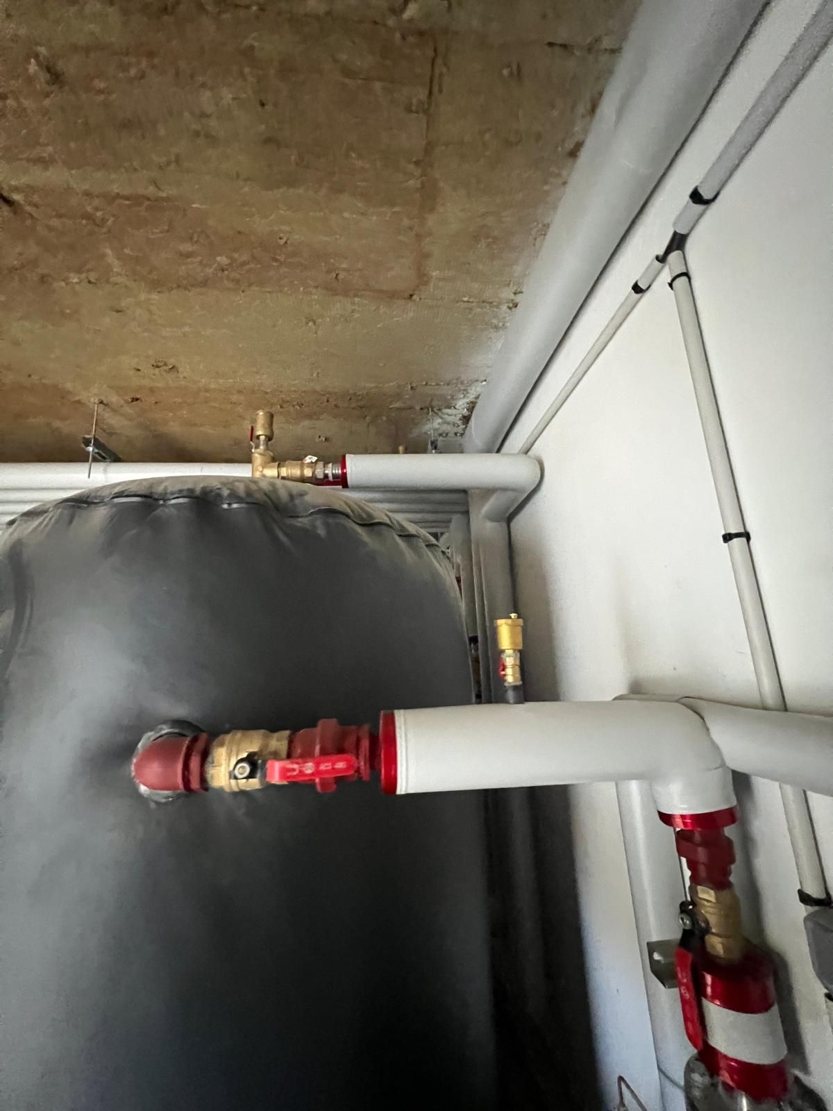 Tuyaux reliés à une cuve à eaux noires, avec vannes en laiton et rouges. Les tuyaux sont blancs et fixés au mur.