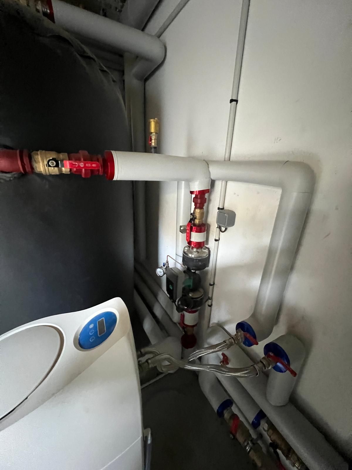 Tuyaux et vannes dans un local technique. Tuyaux rouges et blancs avec un réservoir gris foncé.