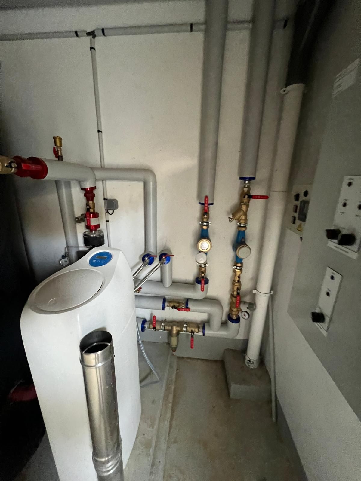 Système de plomberie et de chauffage dans une buanderie avec tuyaux, vannes, adoucisseur d'eau et conduit de cheminée.