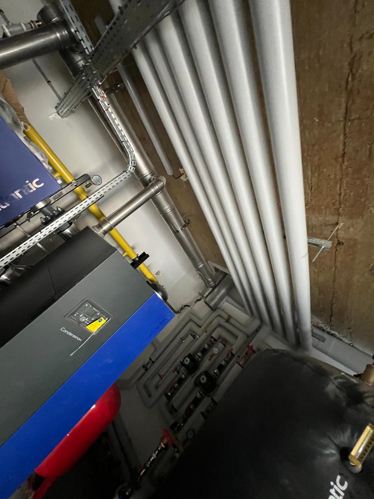 Tuyauterie et équipements mécaniques installés en milieu industriel. Couleurs majoritairement grises, blanches et noires.