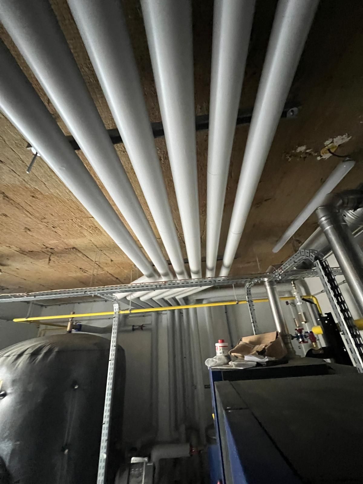 Des tuyaux recouverts d'un isolant blanc courent au plafond, laissant apparaître des équipements en dessous.