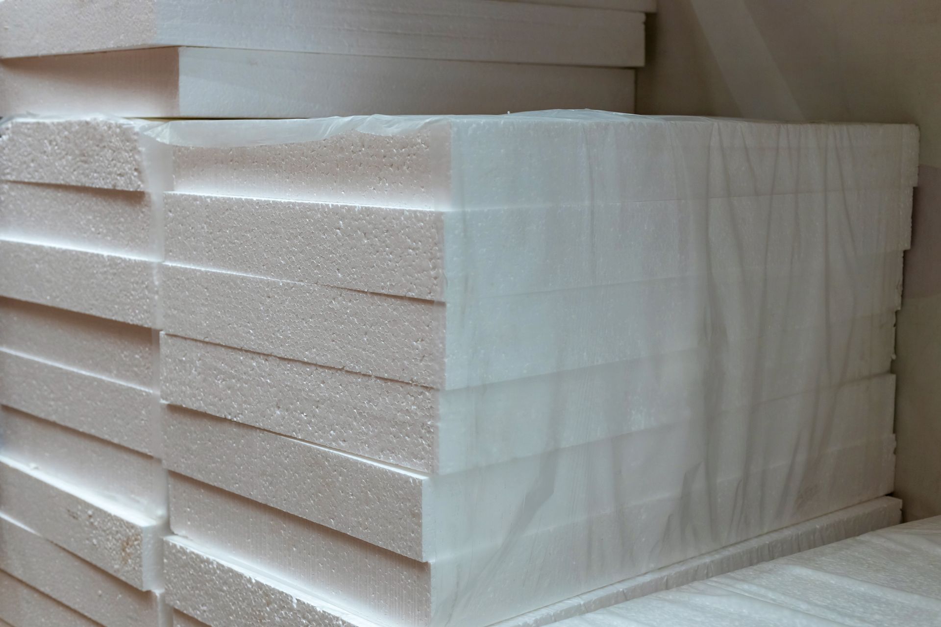 Pile de panneaux isolants en mousse blanche enveloppés dans du plastique transparent.