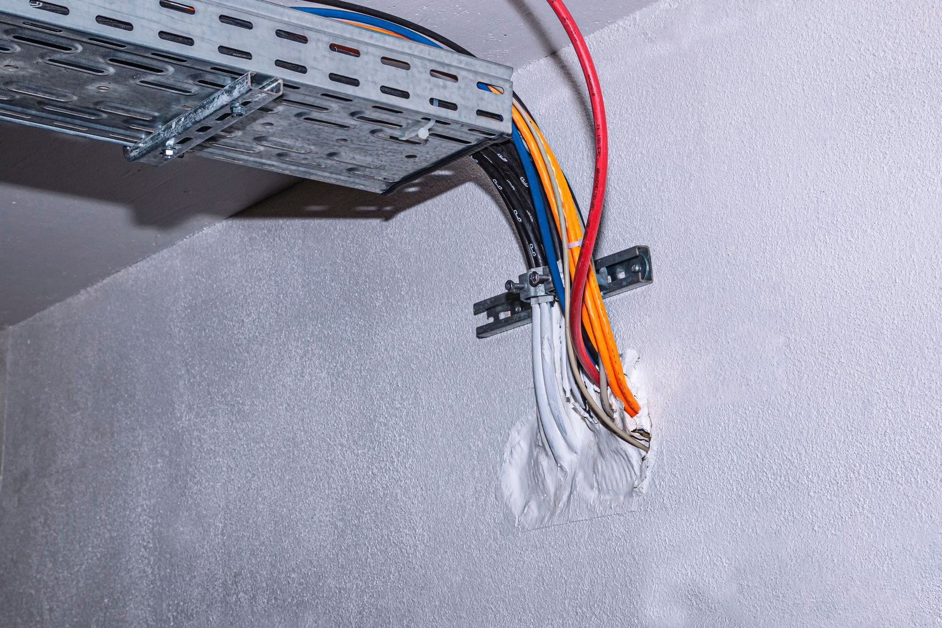 Chemin de câbles avec fils de couleur descendant le long d'un mur.