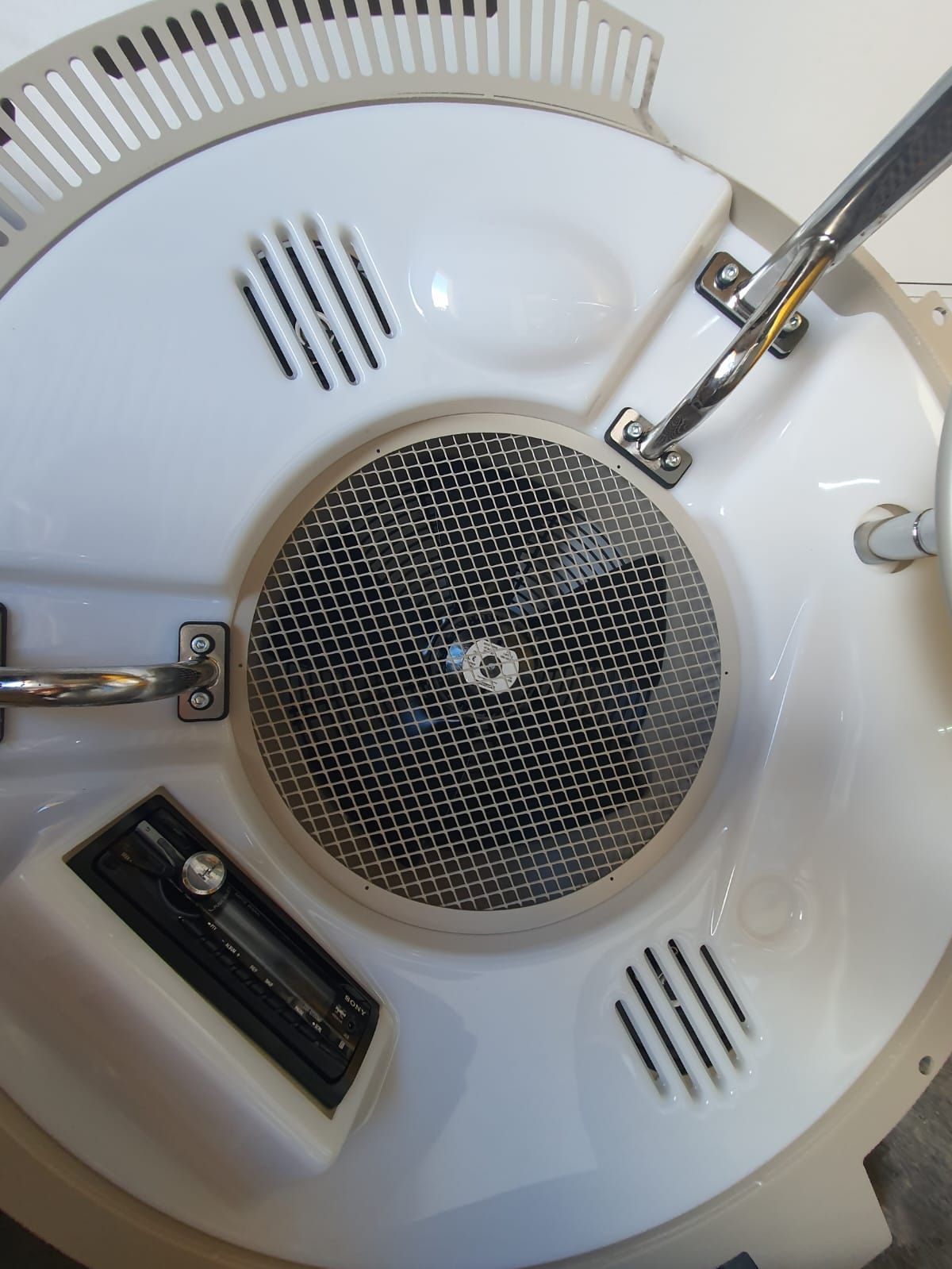 Electrodoméstico circular de color blanco con altavoz revestido de malla, manijas cromadas y panel de control.