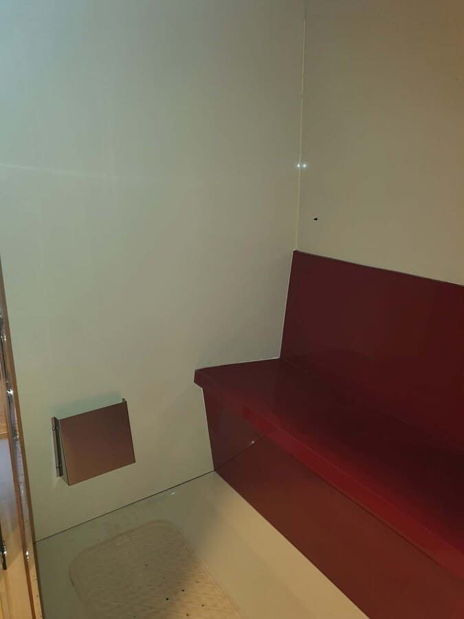 Asientos rojos en la esquina, paredes beige y pequeña ventilación cuadrada.