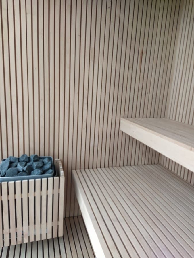 Interior de sauna de madera con bancos, paredes de listones y un calentador relleno de piedras.