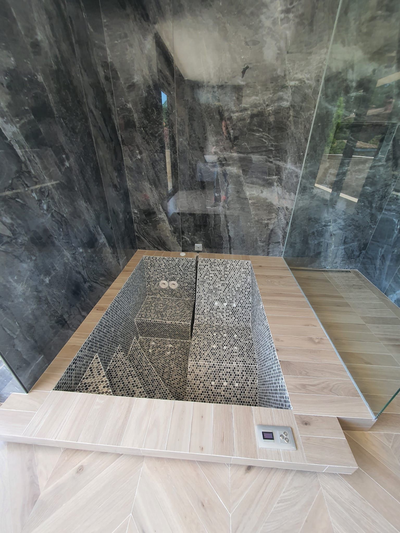 Sauna con piso de madera con una pieza central oscura y texturizada; pared de vidrio a la derecha; pared de hormigón detrás.