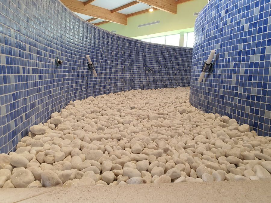 Camino curvo con piedras blancas y paredes de azulejos azules; techo de madera.