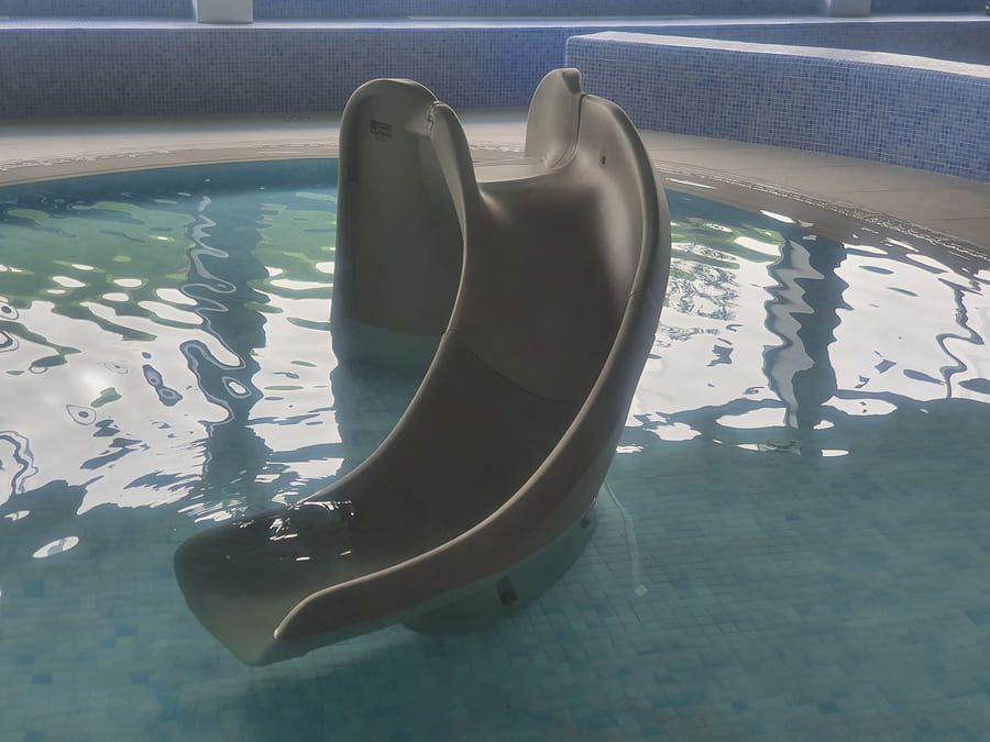 Tobogán de piscina en una piscina de agua, tobogán beige con agua azul.