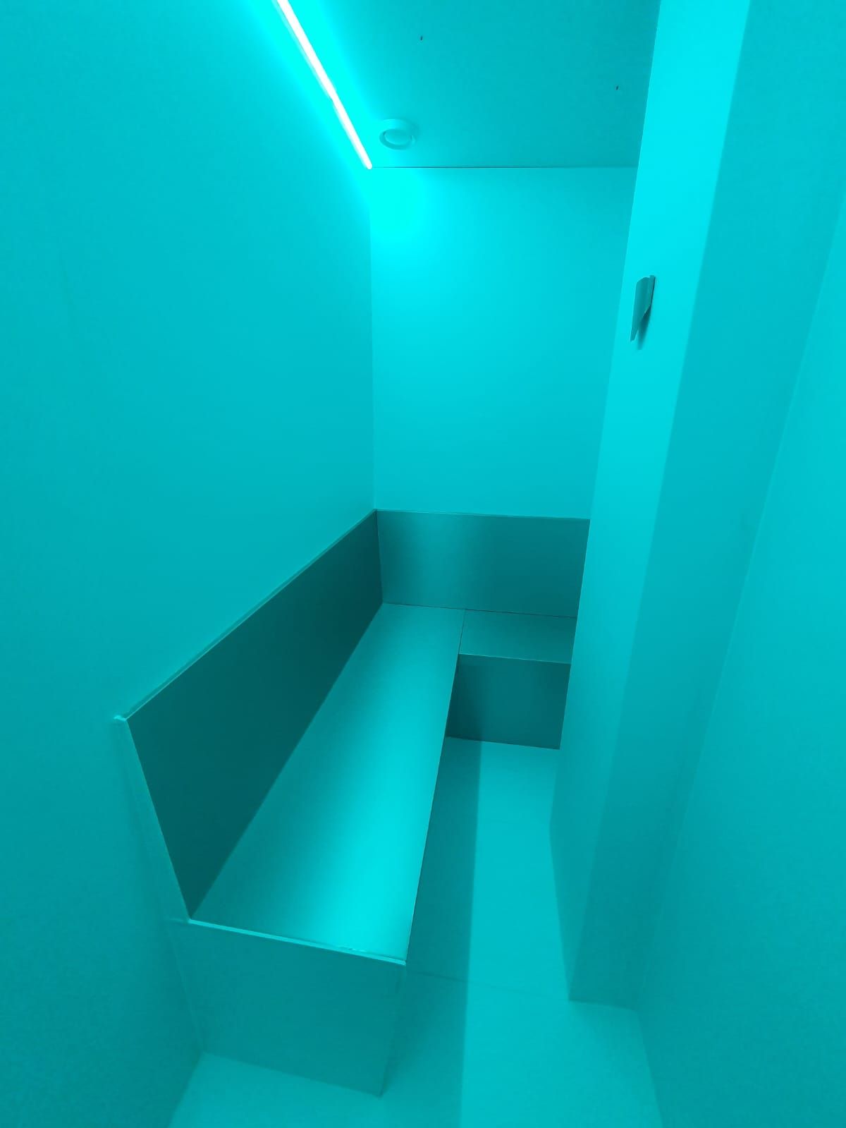 Una habitación de color turquesa con asientos incorporados a lo largo de dos paredes; una lámpara lineal en la parte superior.