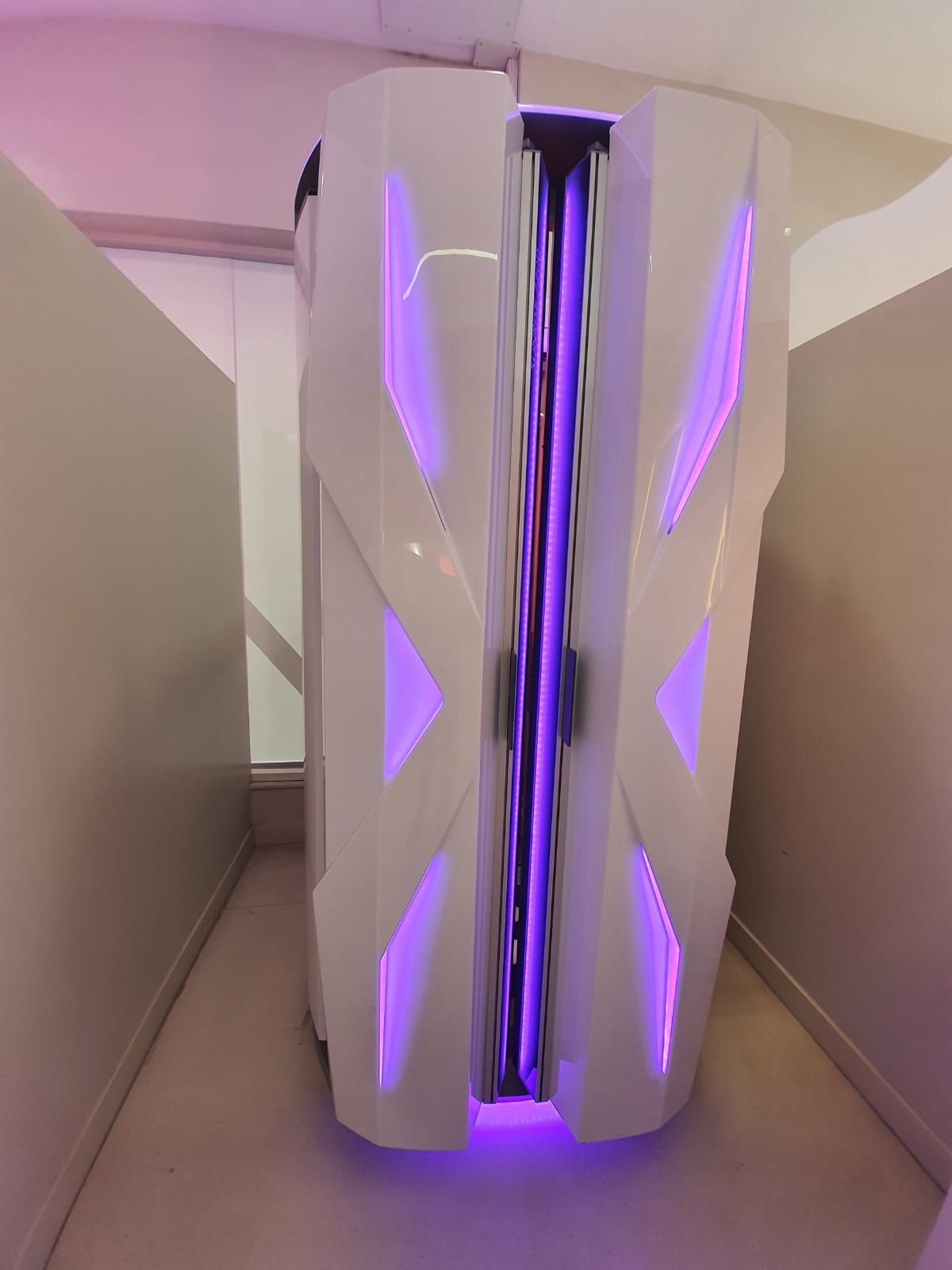 Cabina de bronceado blanca y morada en una habitación estrecha y bien iluminada.