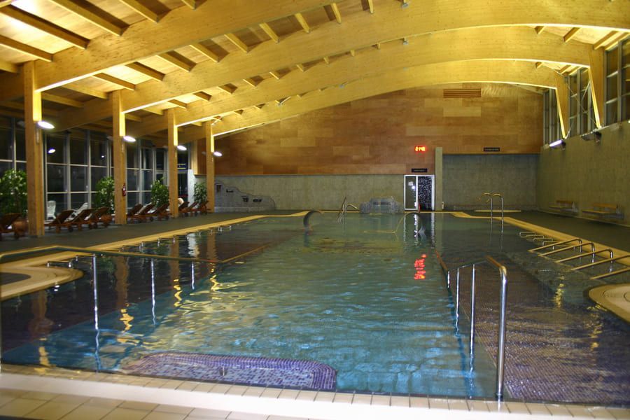 Piscina cubierta con techo de vigas de madera, agua y bordes de baldosas.