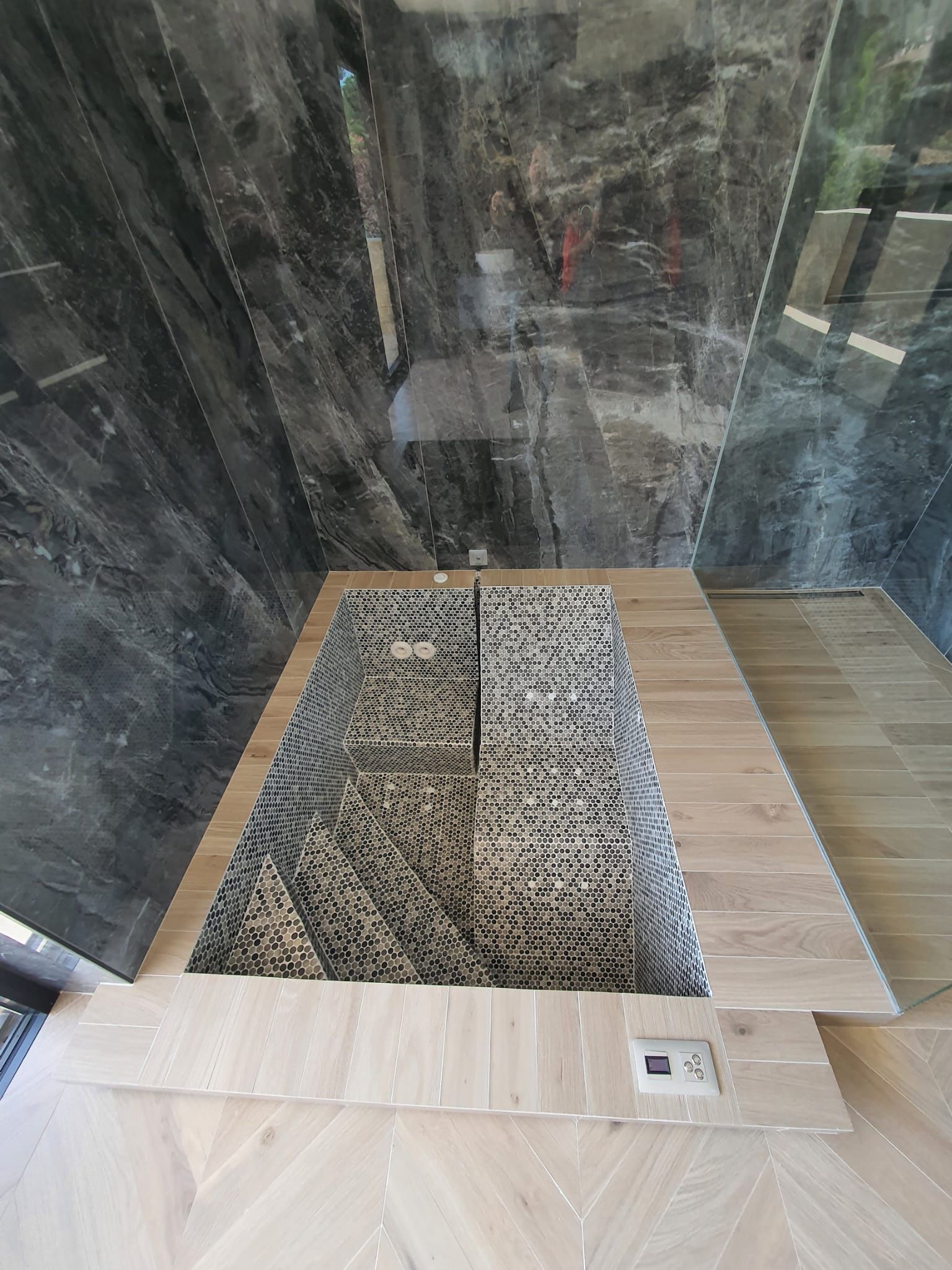 Baño con base de ducha y salpicadero símil piedra, rodeado de suelo de madera.